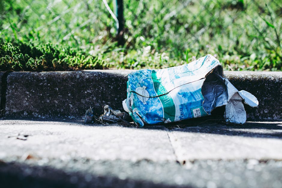 A large heap of black rubbish bags stacked against a modern building with a tiled exterior, with some filled with household waste and others appearing slightly torn or bunched. Among the bags, several clear plastic bottles and smaller pieces of debris are visible, adding to the cluttered appearance. In the background, part of the urban environment can be seen, with a partly cloudy sky overhead, suggesting natural daylight. Graffiti in red spray paint reading 'XEND' is visible on the wall behind the rubbish, indicating possible unauthorized waste disposal or a local environment issue. The scene captures an instance of waste accumulation that could be addressed through professional rubbish removal services, such as those provided by Rubbish Collection Enfield, highlighting the importance of proper waste management and adherence to local rubbish rules, especially in an urban setting where on-site clearance or alternative disposal methods may be necessary to maintain cleanliness and compliance.